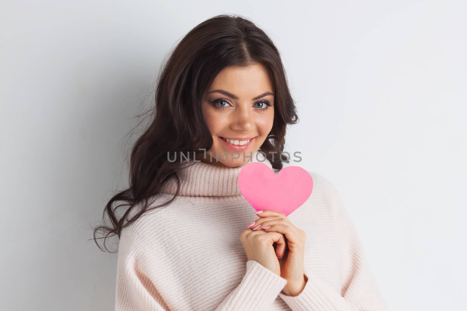 Beautiful young brunette woman holding pink paper heart, looking at camera