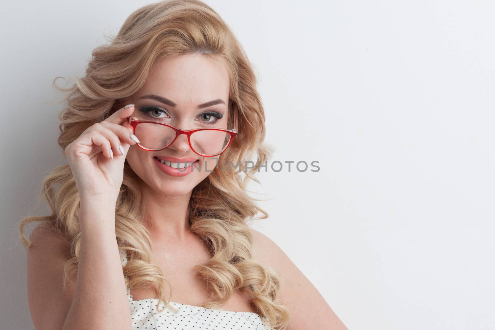 Glamorous green eyed blond woman with long curly hair wearing glasses looking directly at the camera on white