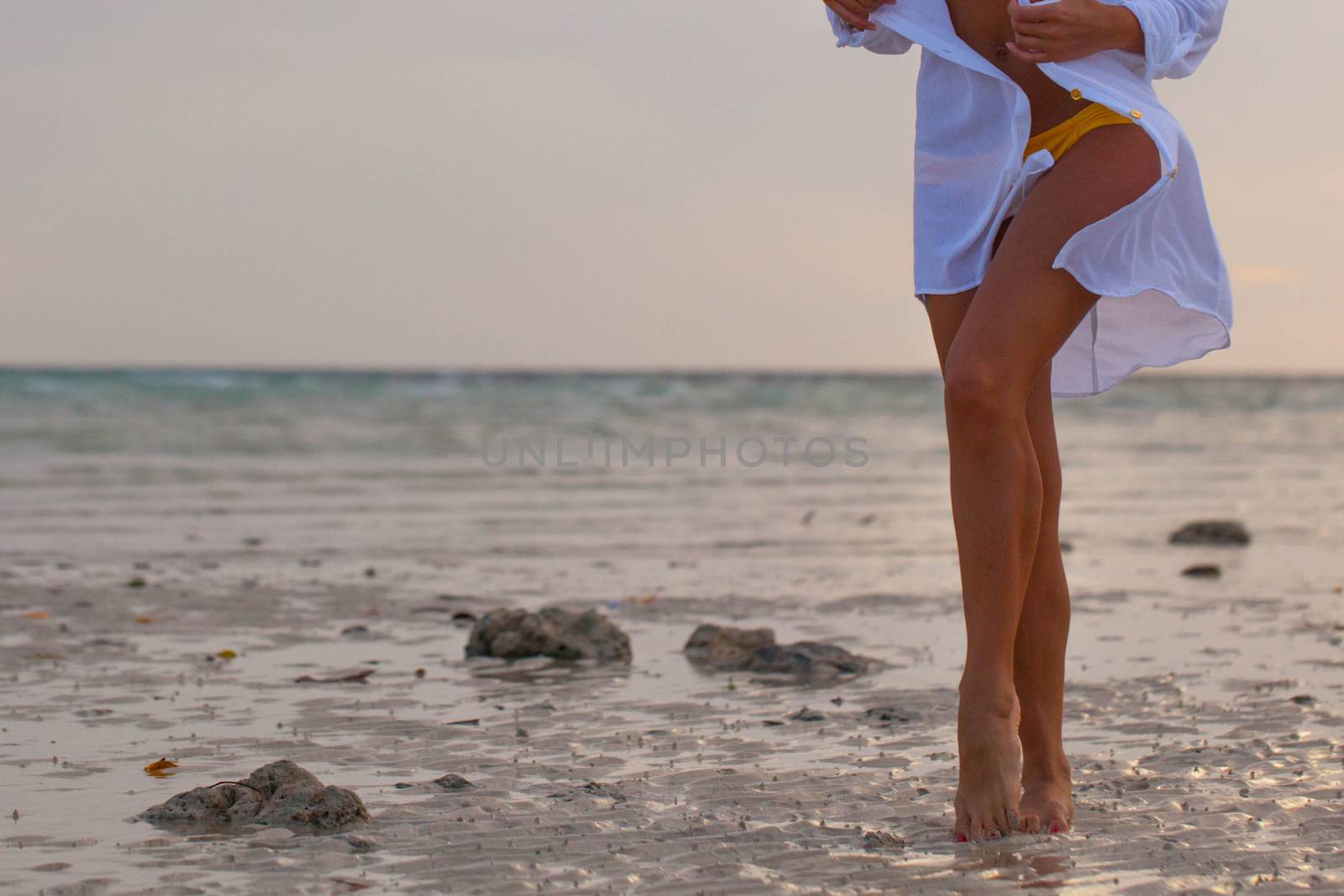 Woman in bikini and white shirt walking on beach at sunset