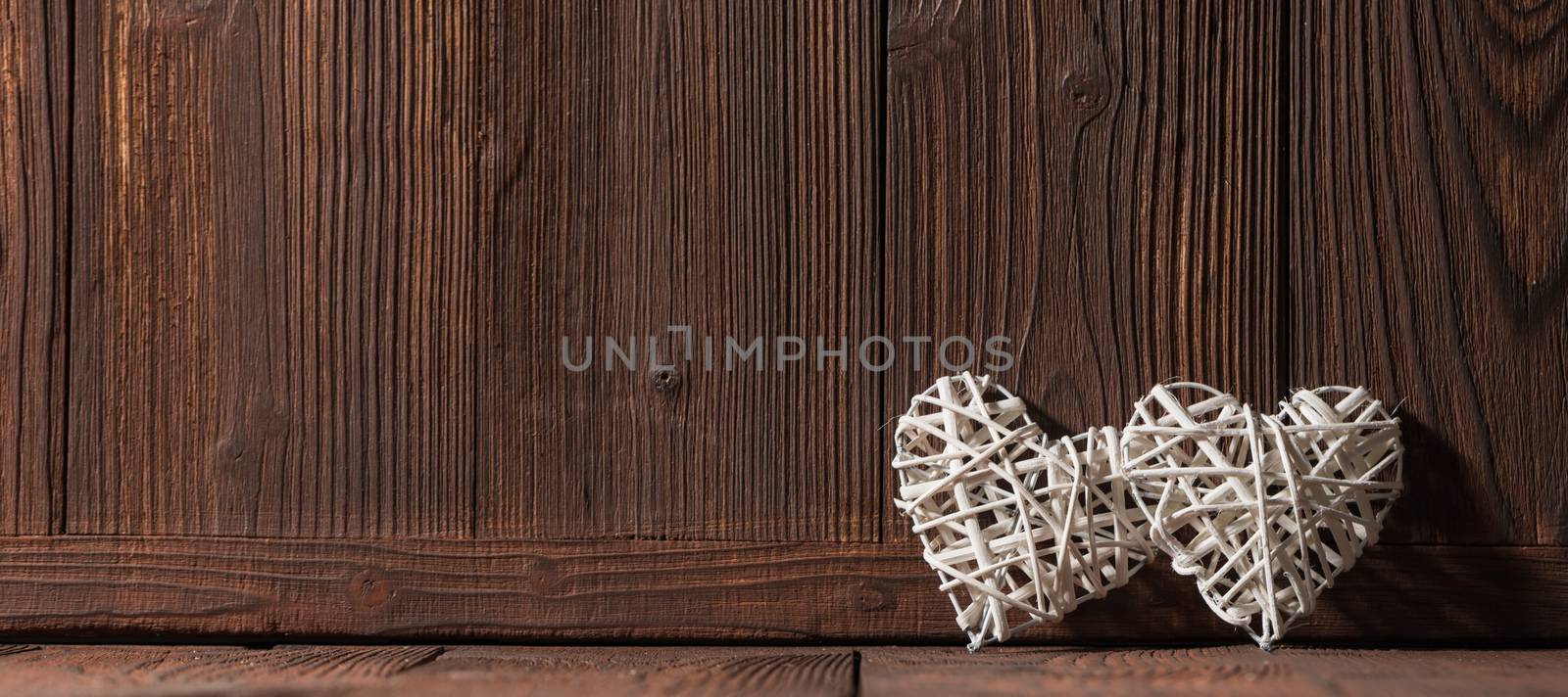 Two wicker hearts on brown wooden background