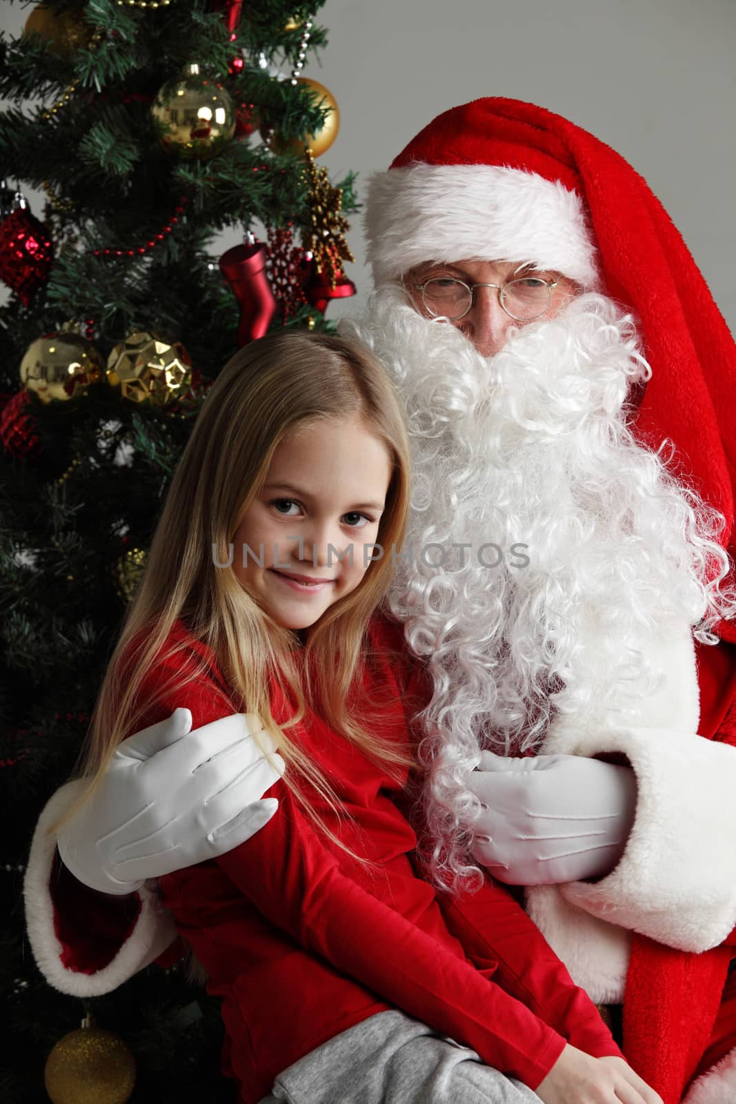 Portrait of smiling little girl sitting on santa claus knees near christmas tree