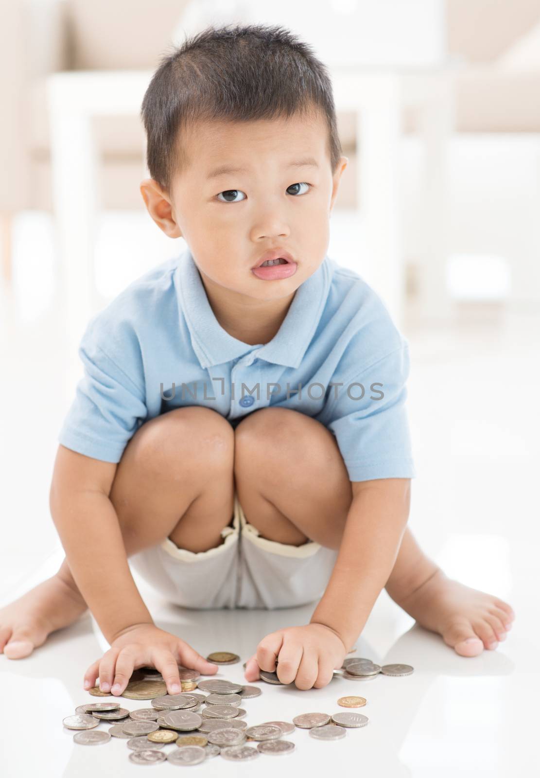 Asian preschool boy saving coins at home. Child education fund concept. 