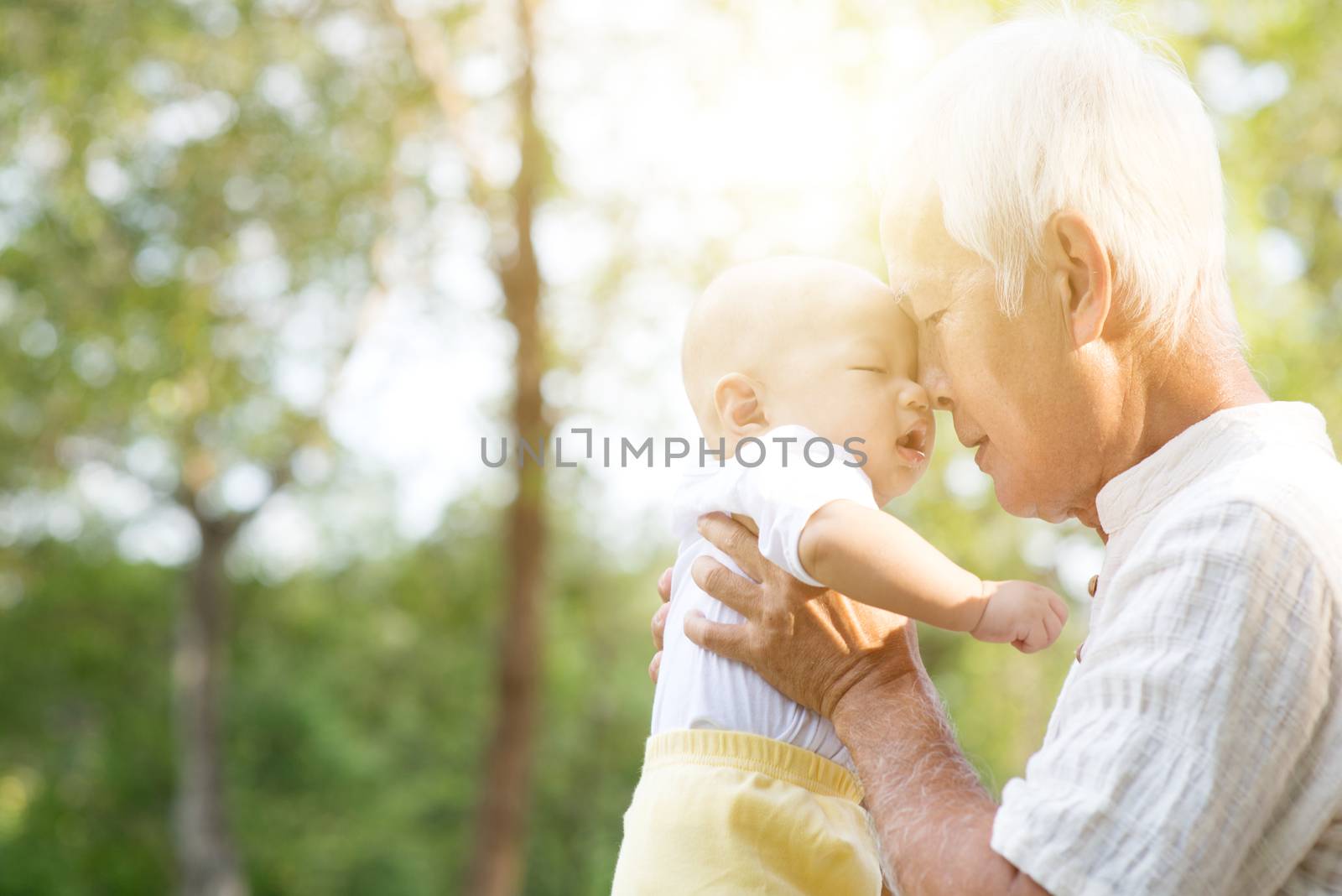 Grandfather kissing baby grandson at outdoor park, Asian family, life insurance concept.