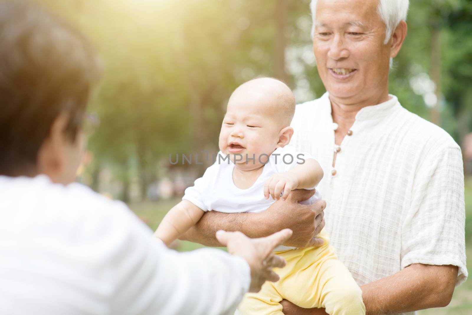 Grandparents holding baby grandchild at outdoor park, Asian family, life insurance concept.