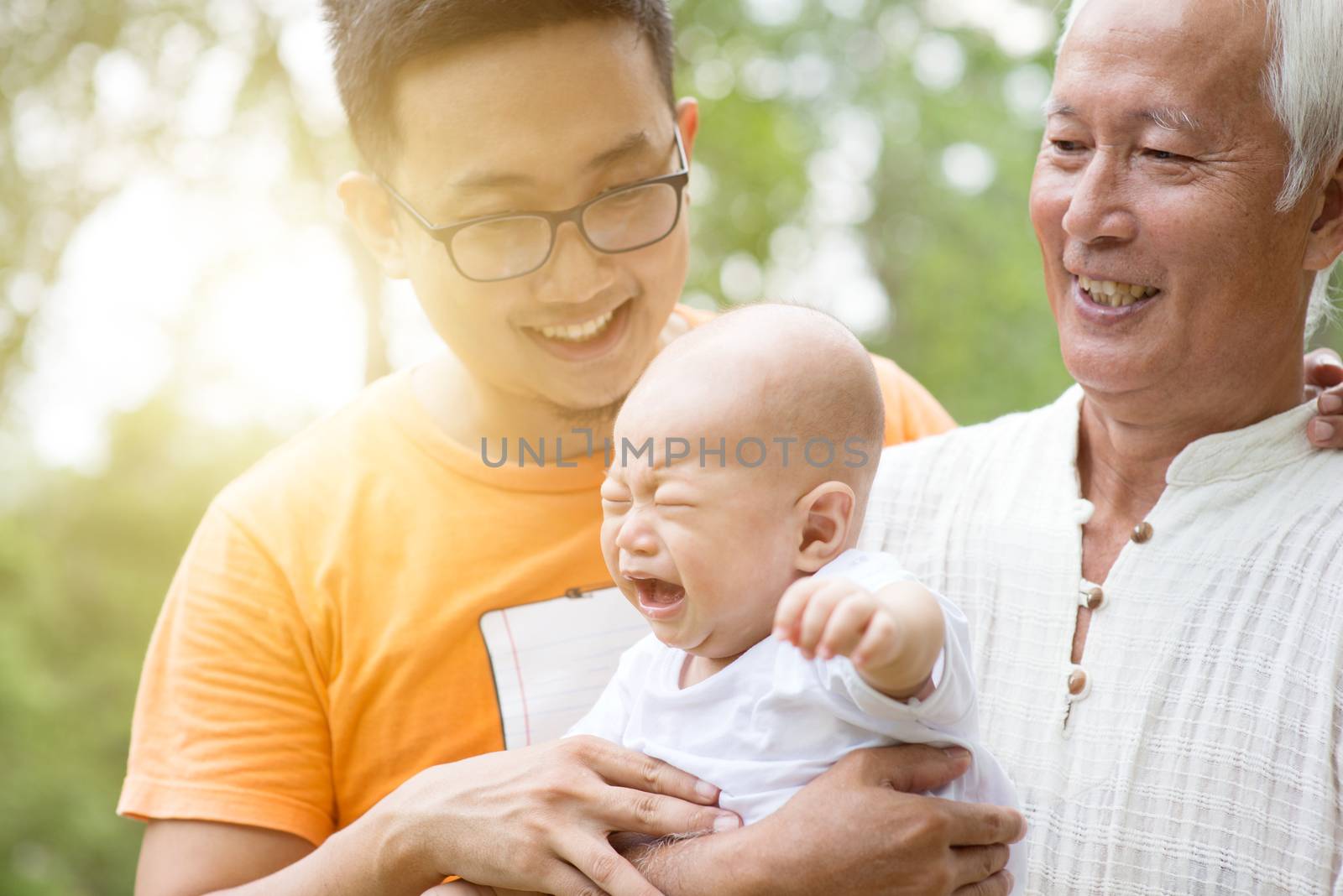 Happy grandfather, father and crying baby grandchild at outdoors park. Asian multi generations family.