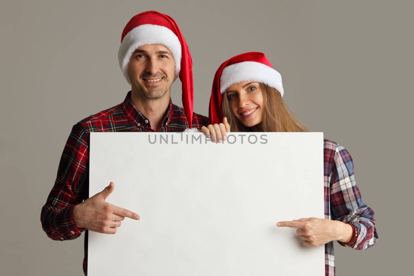 Happy couple in Santa hats holding blank banner and pointing at copy space