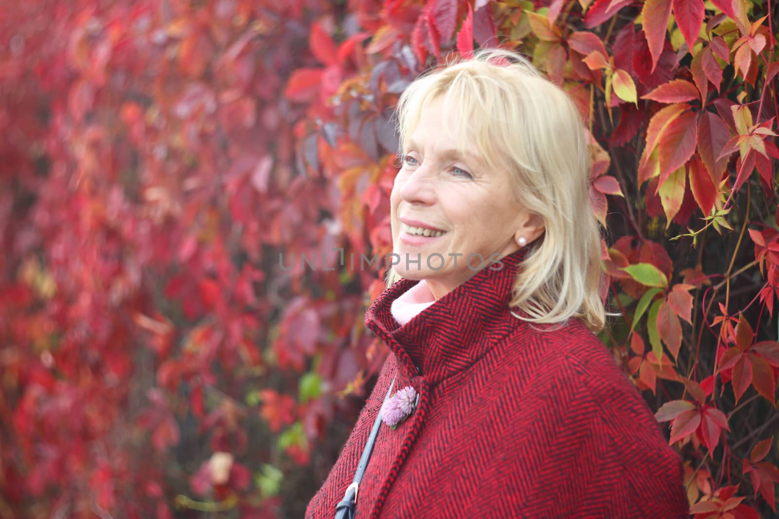 Happy smiling senior woman in autumn park over red leaves background
