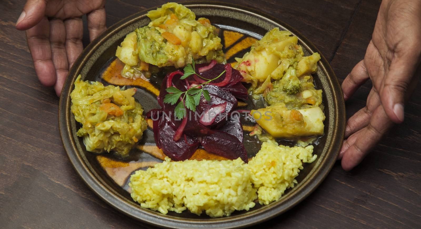 An afro-american man s hands are presenting a plate with vegetable stew and salad of red beetroot.