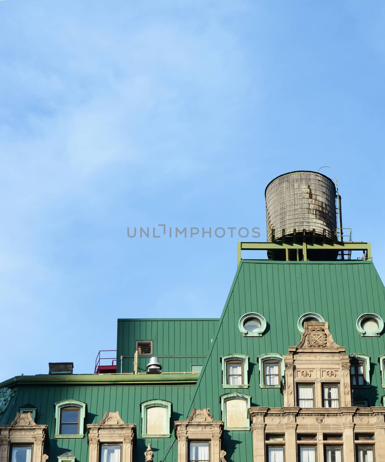 Water tower on the rooftop of a New York City building with a distinctive green roof, against a blue sky