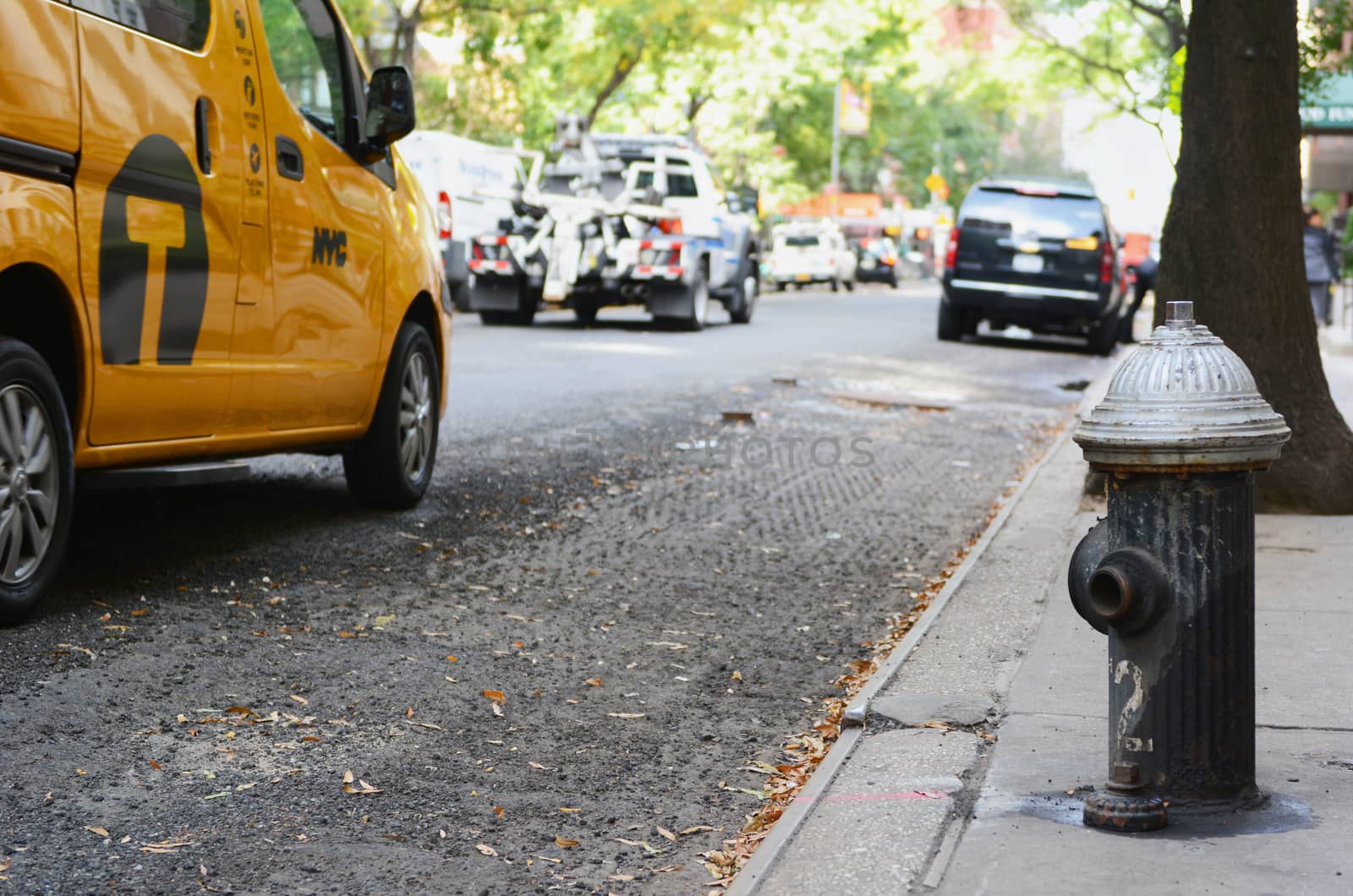Black fire hydrant on the edge of a New York city sidewalk. A yellow taxi cab and a police tow truck are among the street traffic driving past.