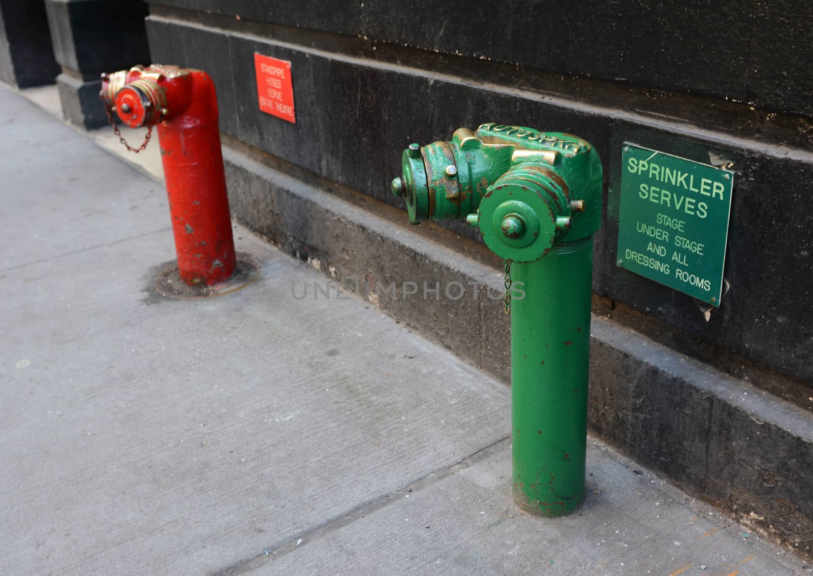 Red and green siamese standpipes on a sidewalk with theatre-related information signs