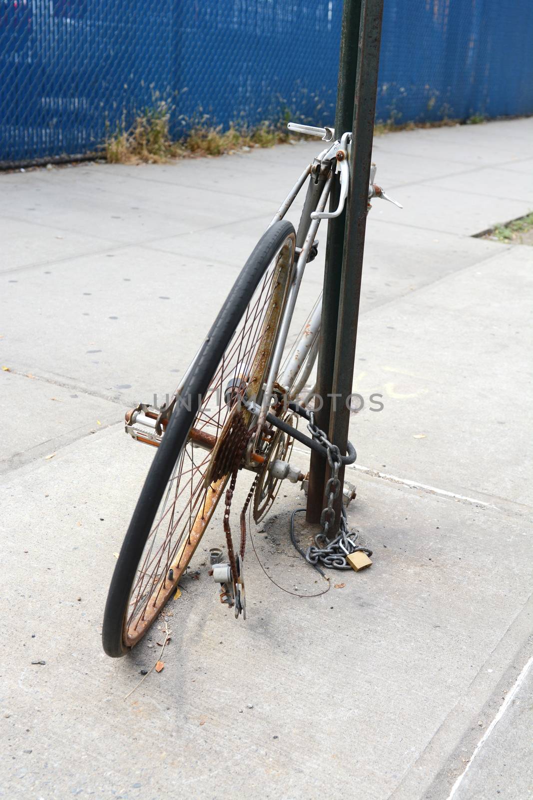 Abandoned broken and rusty bicycle chained to a metal pole on a pavement