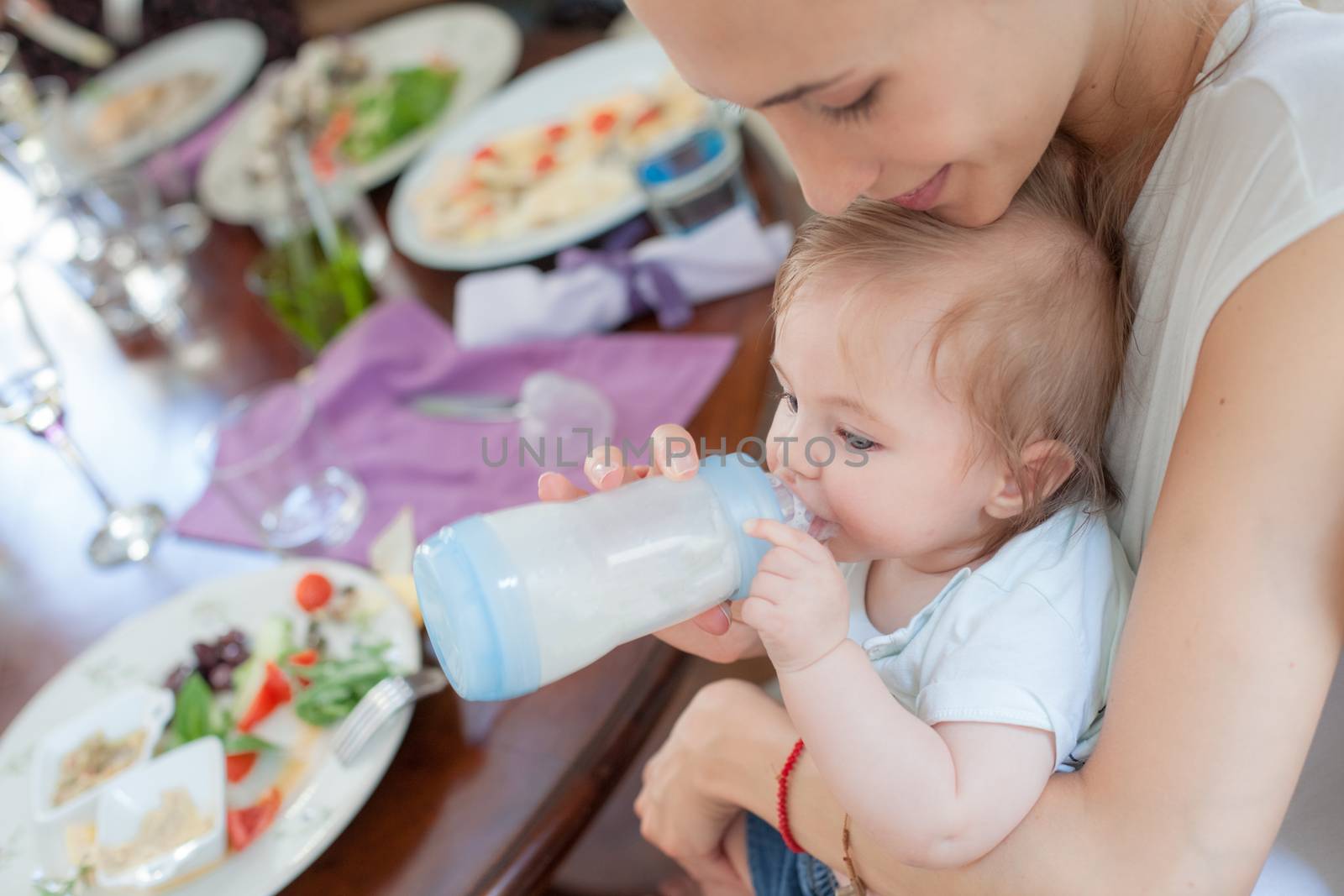 Young beautiful mother is feeding her cute little boy with milk in a restaurant.