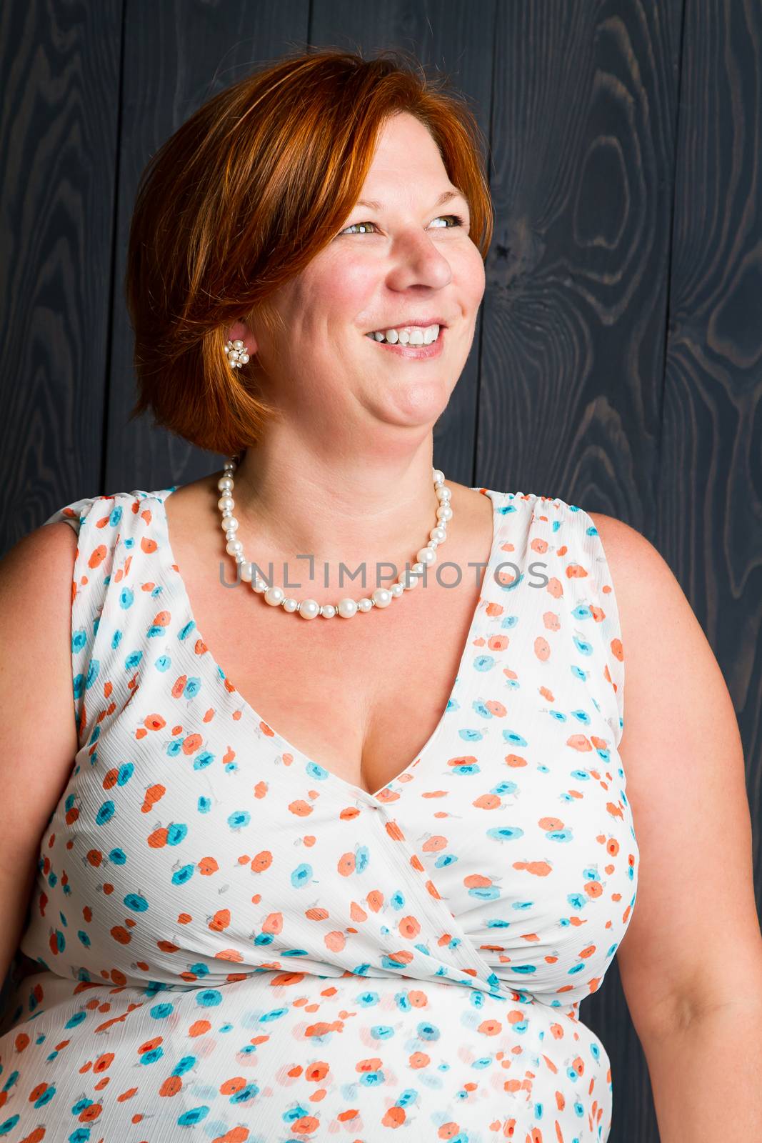 forty something brunette woman wearing a sun dress in front of blue wood panel looking into her right and laughing