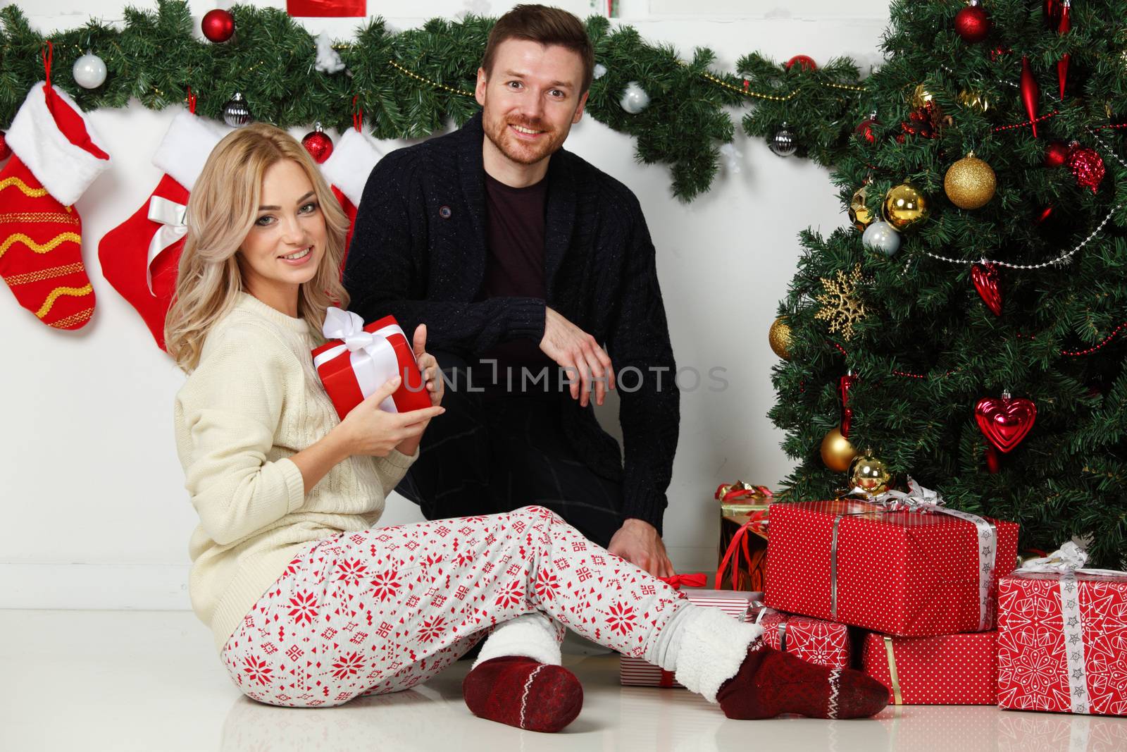 Couple in love sitting next to a nicely decorated Christmas tree, hloding Christmas gifts and smiling