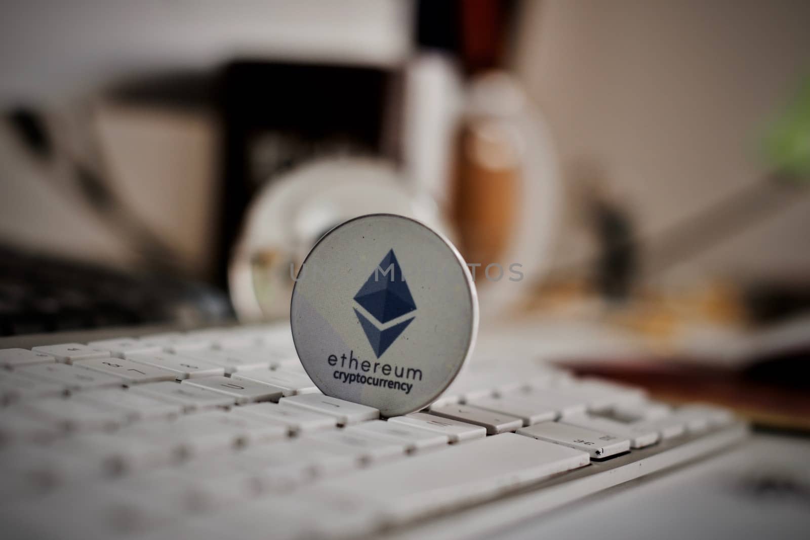 Crypto currency physical grey ethereum token on white keyboard in office.