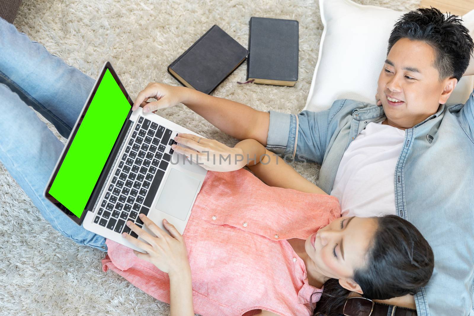 Young Asian Couples lying down and using laptop together in living room of contemporary house for modern lifestyle concept