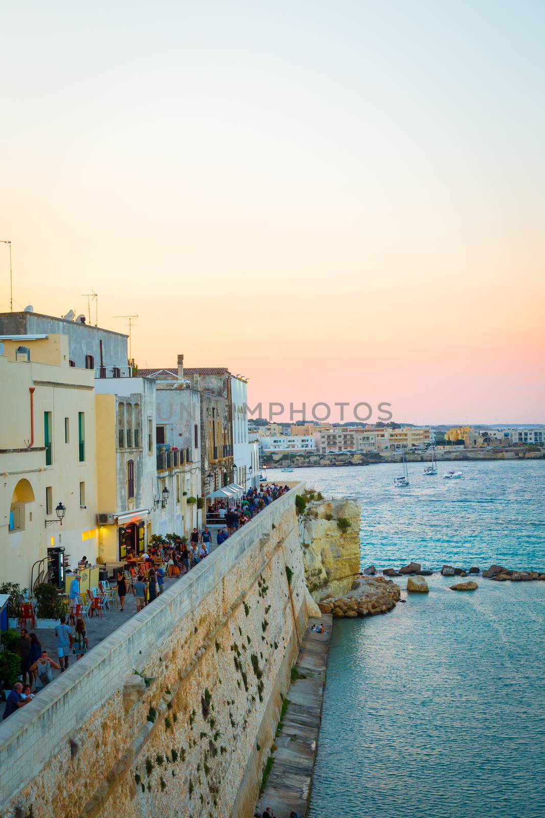 At peak of turistic season, the turist crowd is walking at sunset on the road from the new to the old side of Otranto town