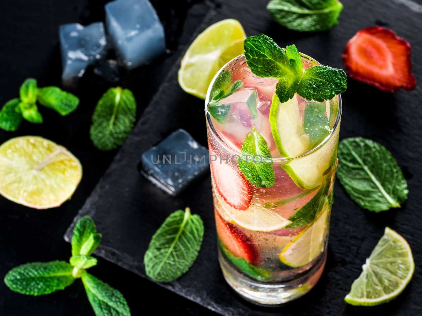 fresh lemonade with strawberry, lime and mint on dark stone background. Cold summer strawberry drink with mint and ice. Strawberry mojito in glass and ingredients