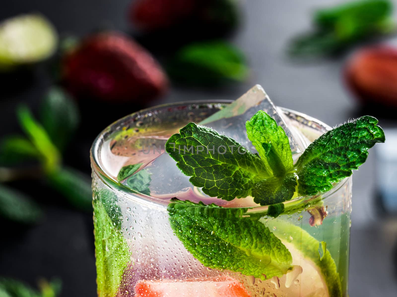 fresh lemonade with strawberry, lime and mint on dark stone background. Cold summer strawberry drink with mint and ice. Strawberry mojito in glass and ingredients