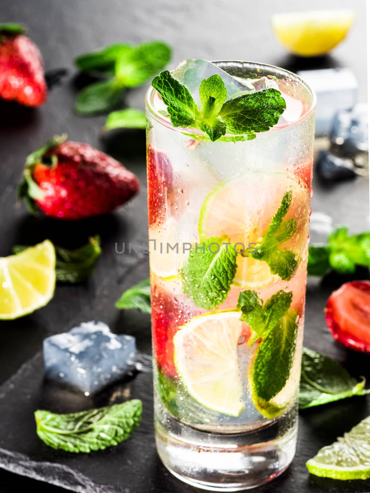 fresh lemonade with strawberry, lime and mint on dark stone background. Cold summer strawberry drink with mint and ice. Strawberry mojito in glass and ingredients. Vertical