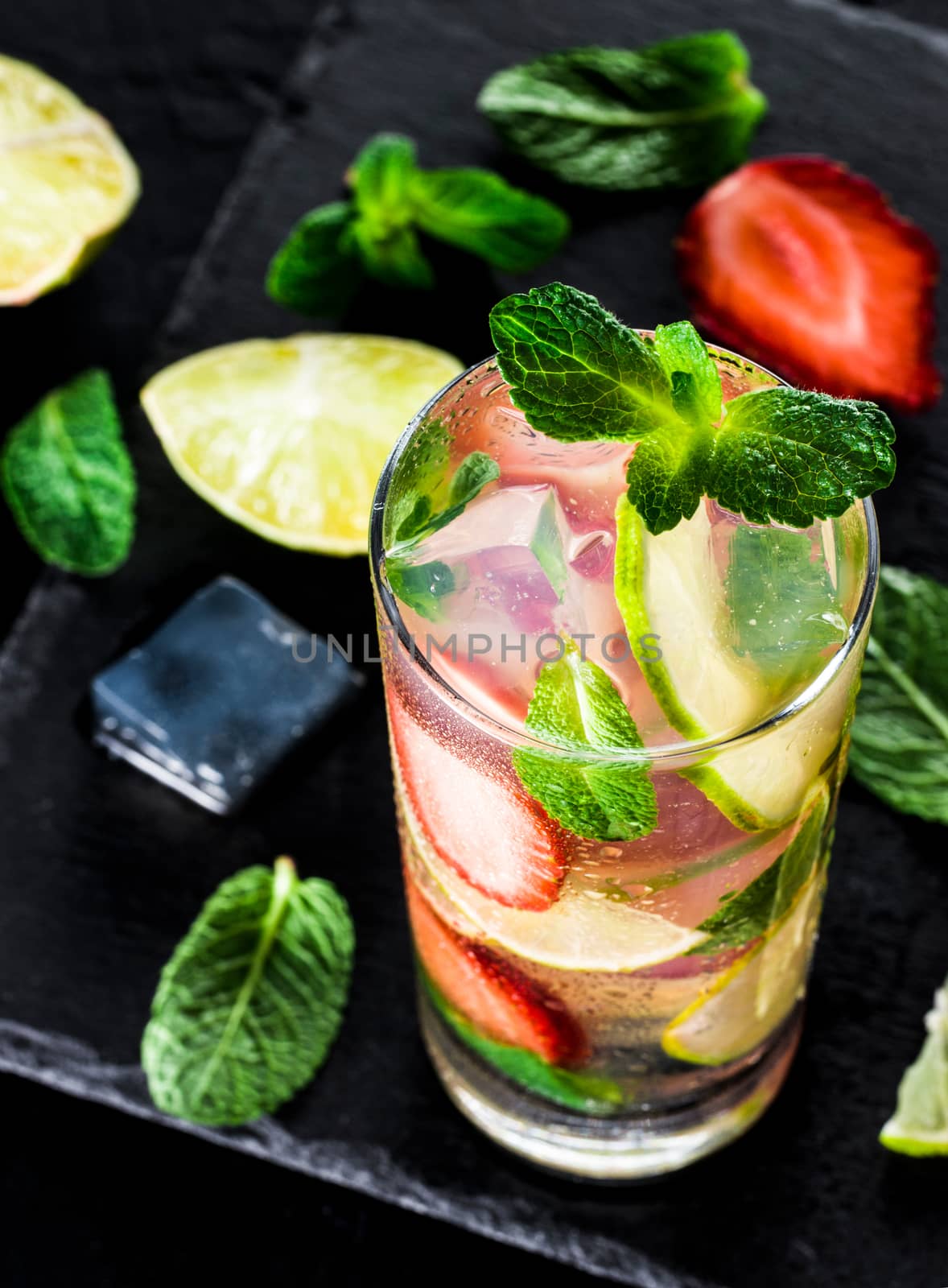 fresh lemonade with strawberry, lime and mint on dark stone background. Cold summer strawberry drink with mint and ice. Strawberry mojito in glass and ingredients. Vertical