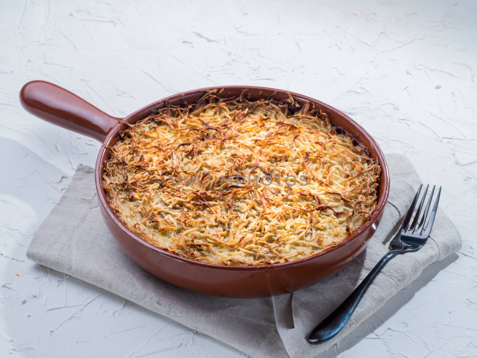 Close up view of appetizing potato casserole with fish, eggs and cream. Potato casserole in serving baking pan on white concrete background