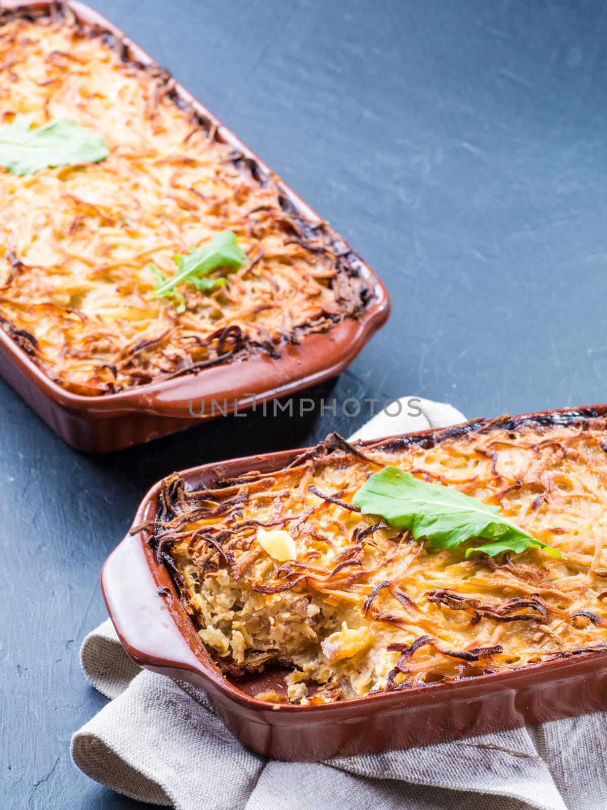 Close up view of appetizing potato casserole with fish, eggs and cream. Potato casserole in serving baking dish on dark concrete background