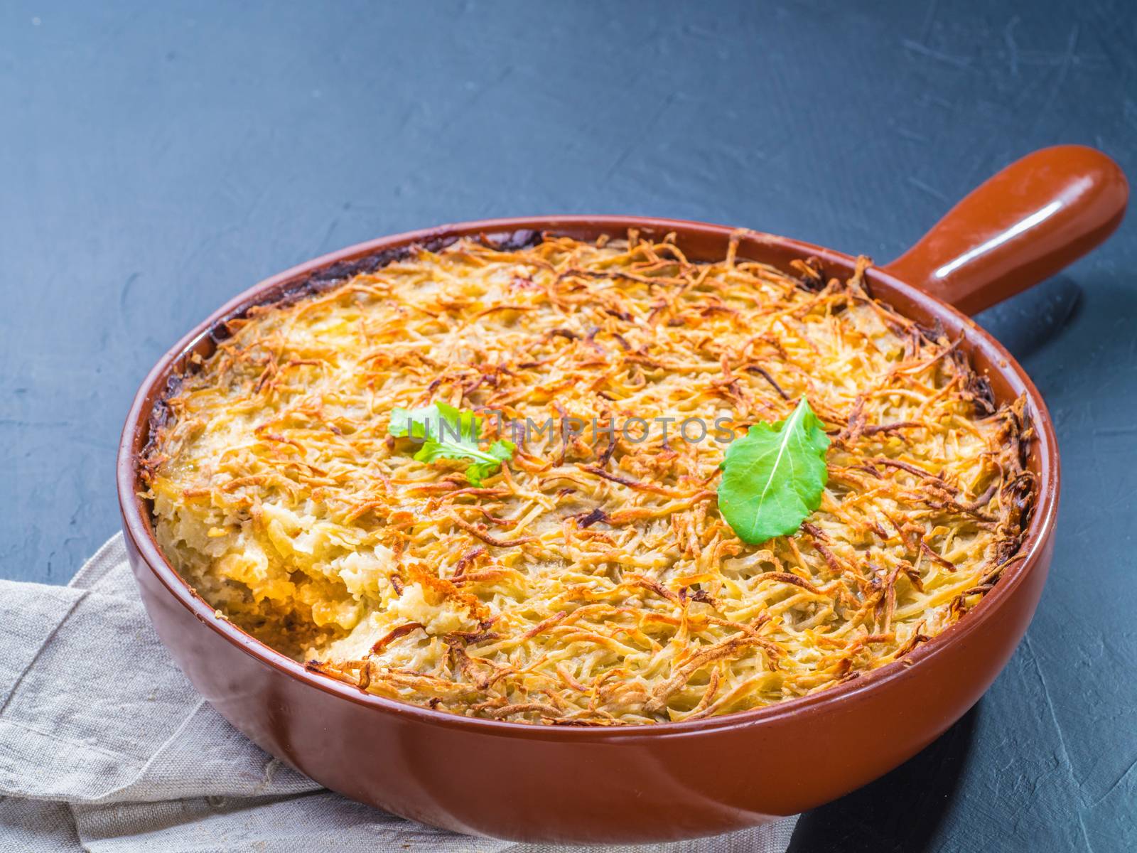 Close up view of appetizing potato casserole with fish, eggs and cream. Potato casserole in serving baking pan on dark concrete background