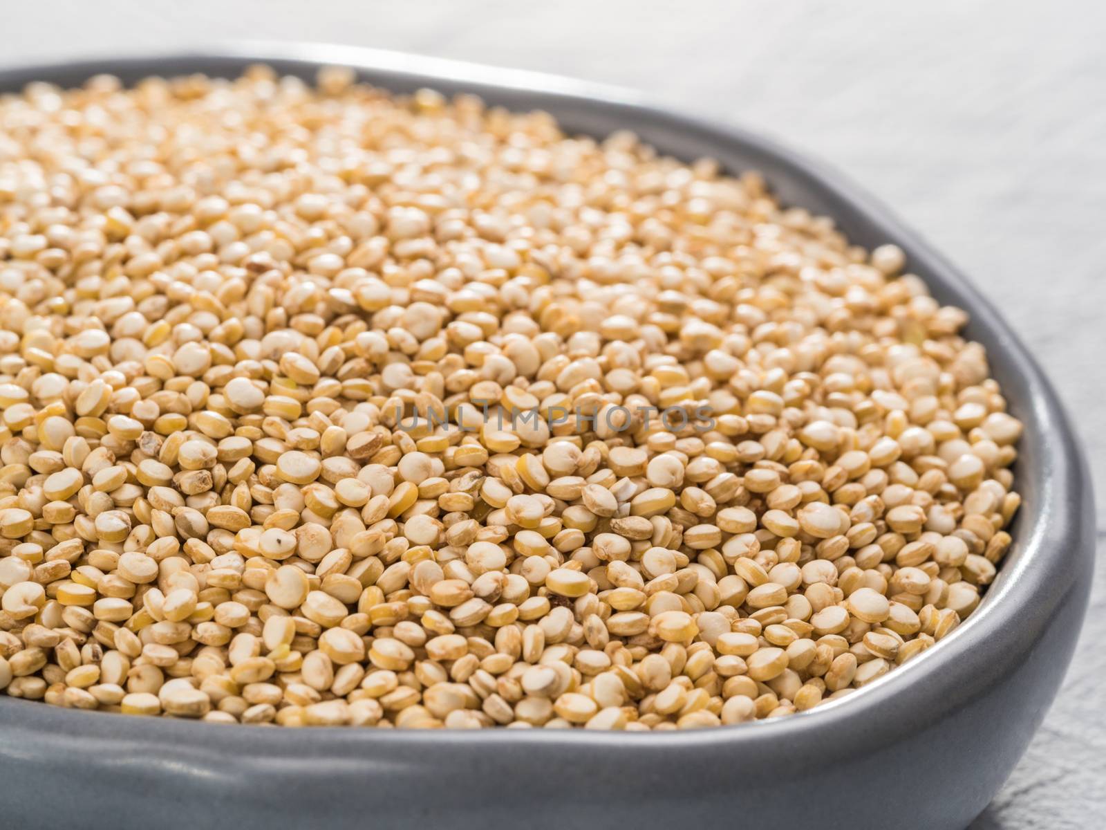 Close up view on dry quinoa in plate on gray concrete background