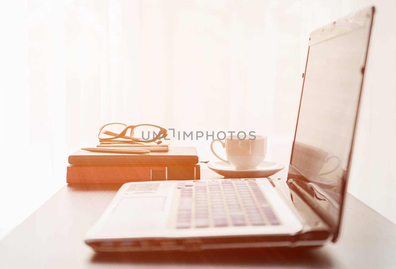 Close up laptop placed on desktop with coffee cup and glasses on book in room at home office