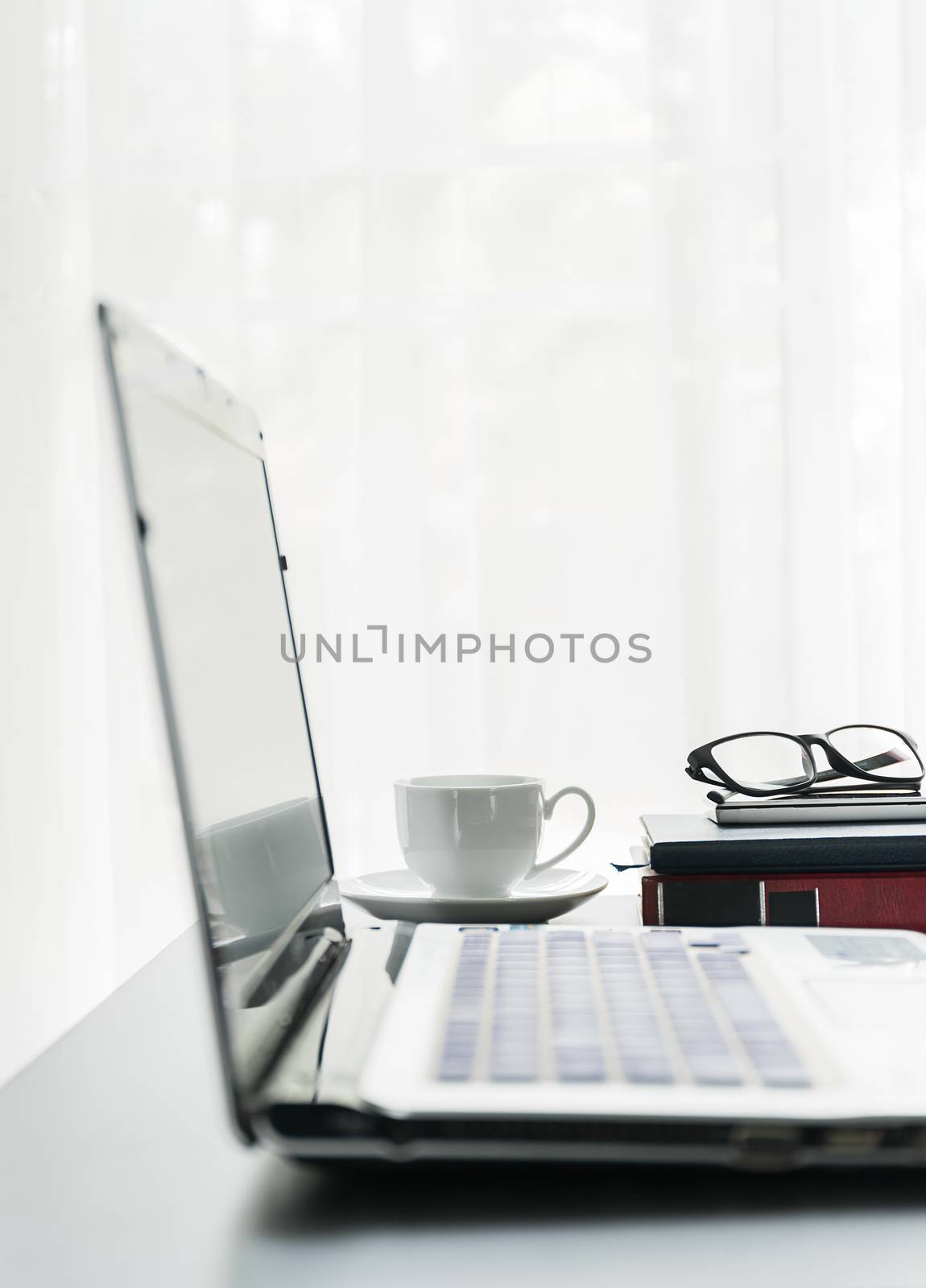 Close up laptop placed on desktop with coffee cup and glasses on book in room at home office