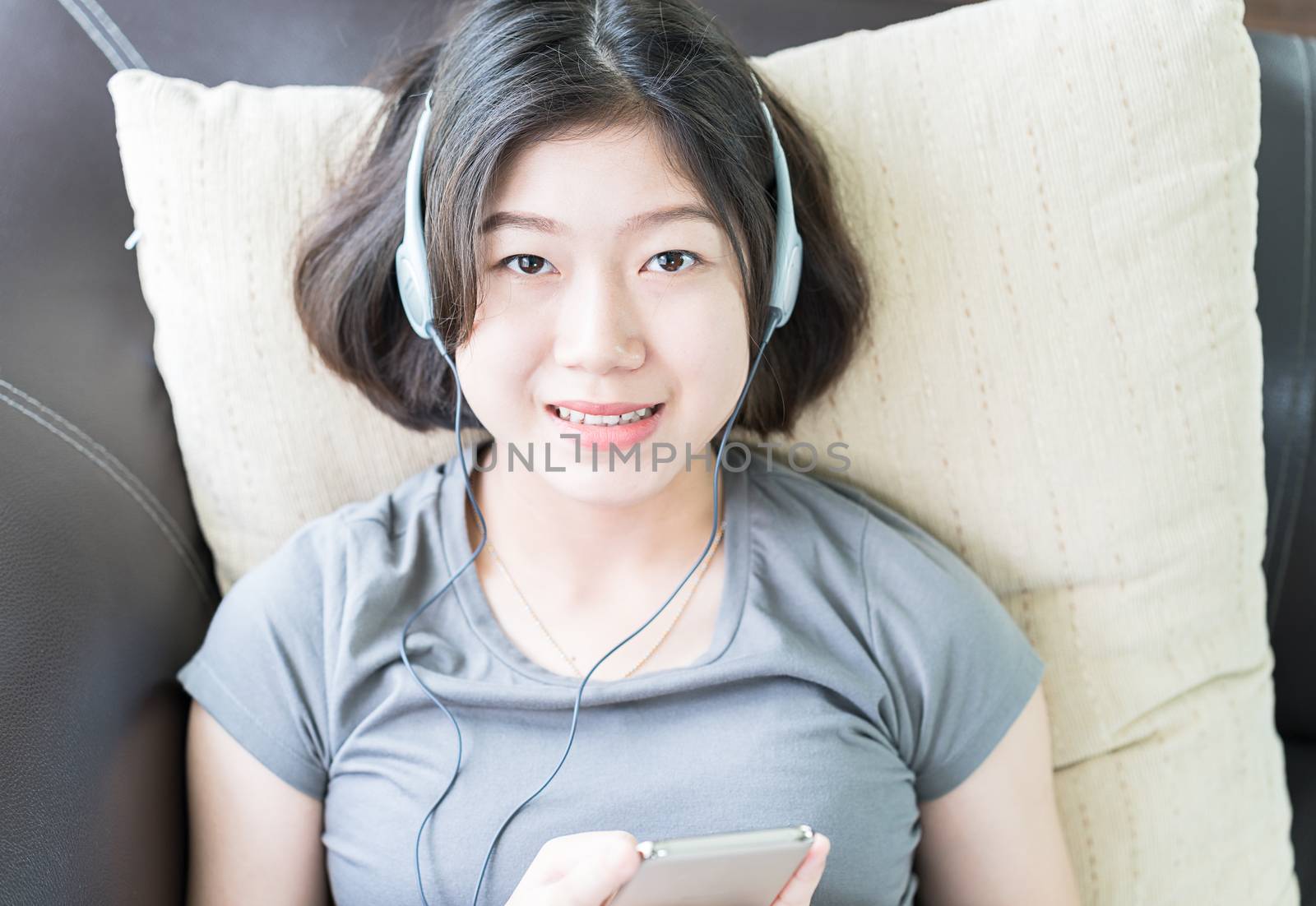 Close up young asian woman short hair listening music from mobile phone on the couch