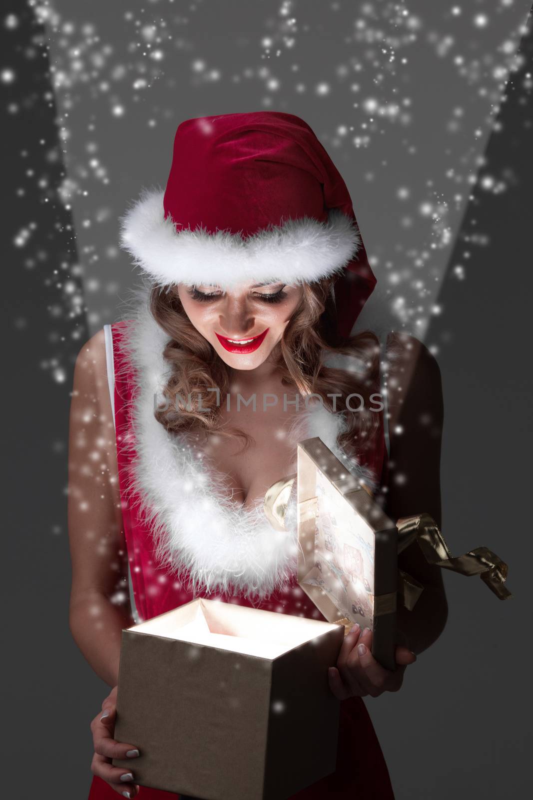 Beautiful woman in Santa Claus style costume looking into glowing Christmas gift box