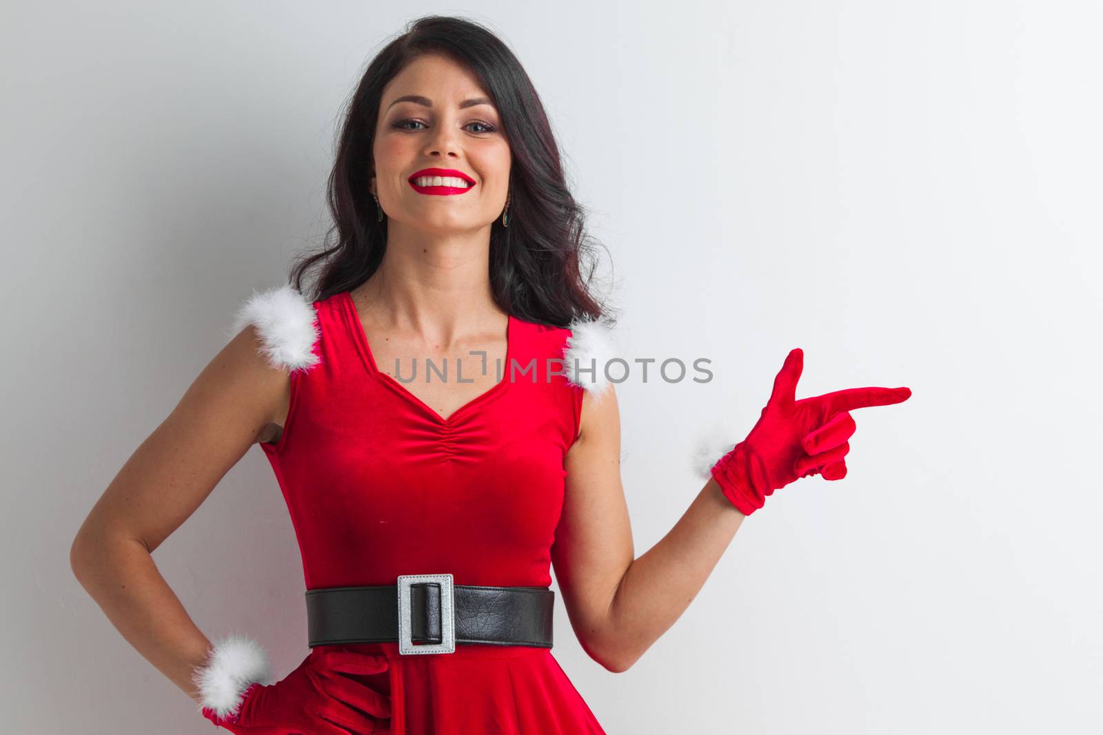 Pretty Pin-up style Santa girl in red hat pointing to white background