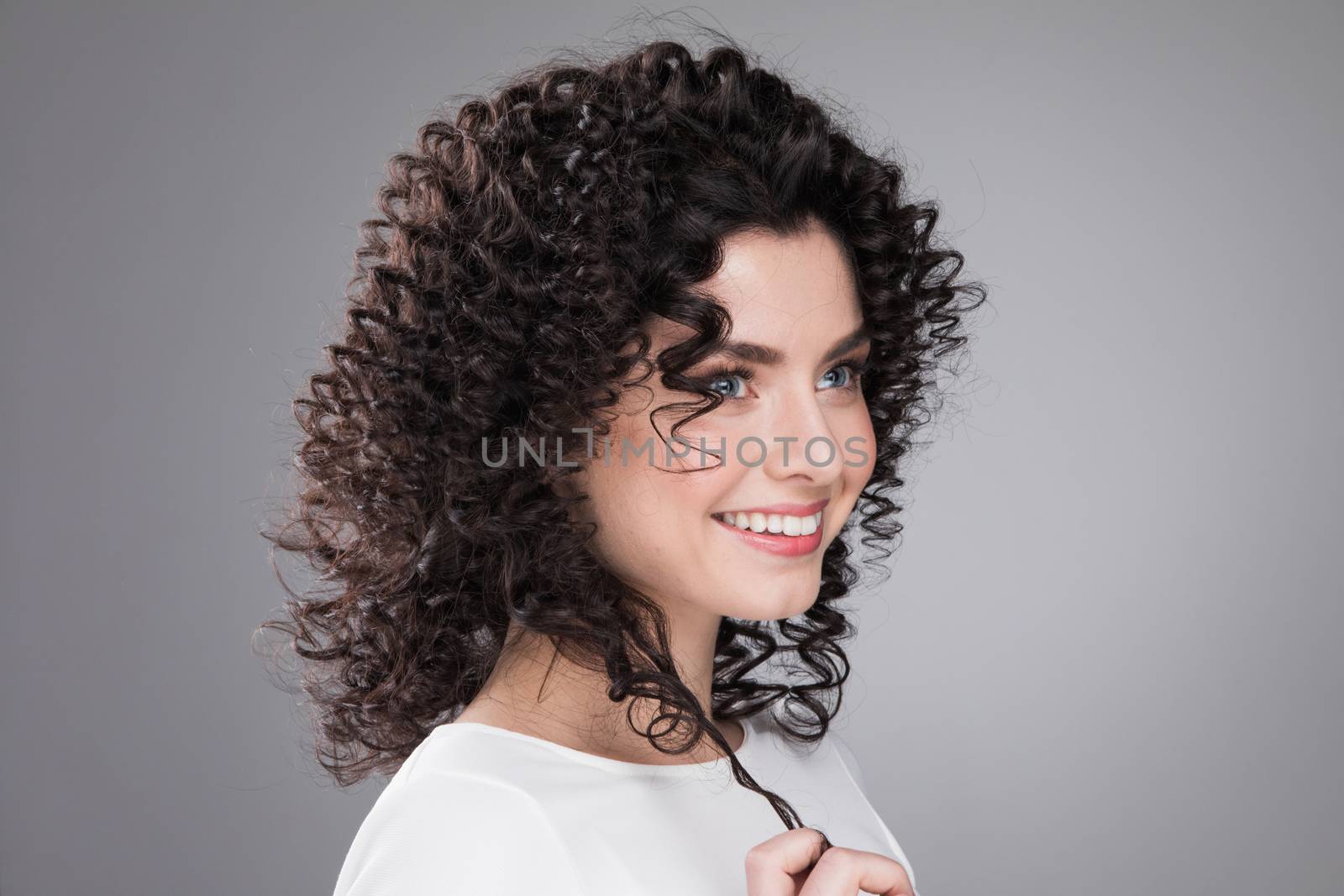 Portrait of amazing beautiful smiling woman with curly hair on gray background with copy space