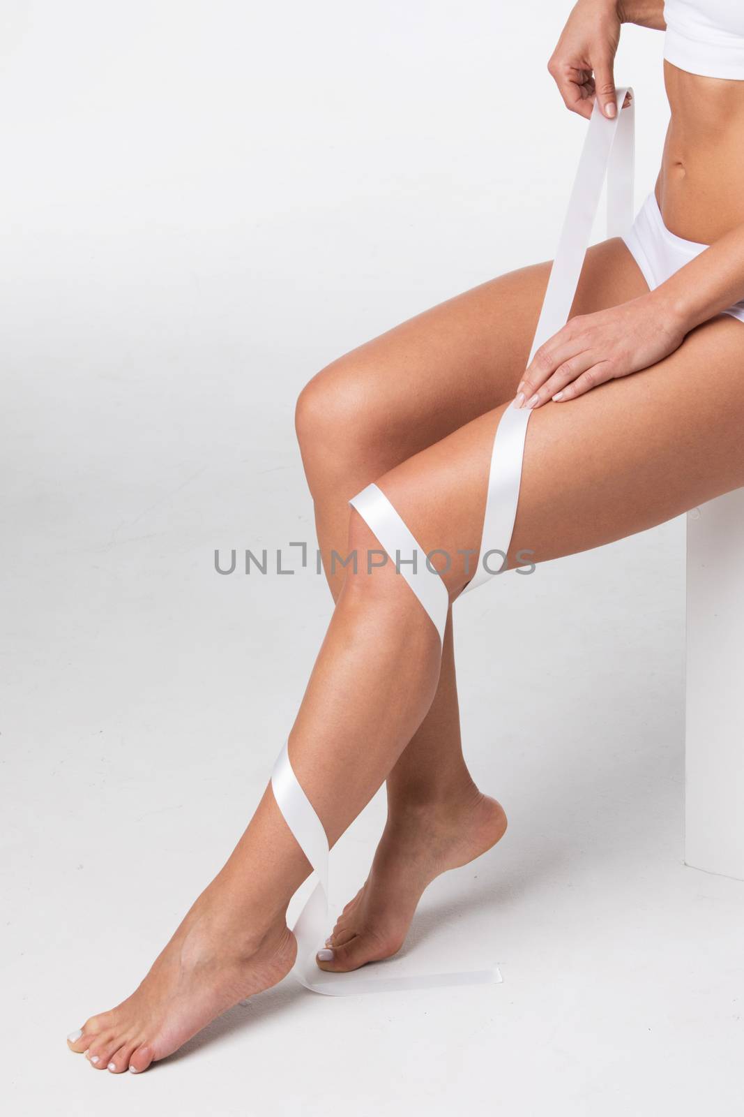 Studio shot of young woman with perfect body with leg wrapped in white ribbon, depilation, varicose concept