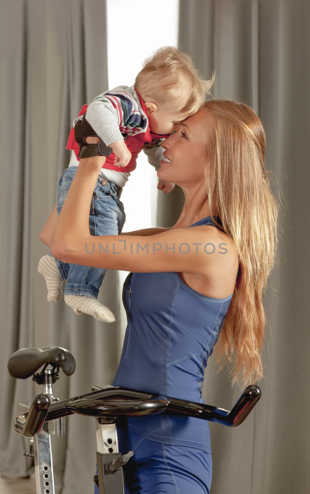 Young beautiful mother having fun embracing her cute little boy with affection in a cycling gym.
