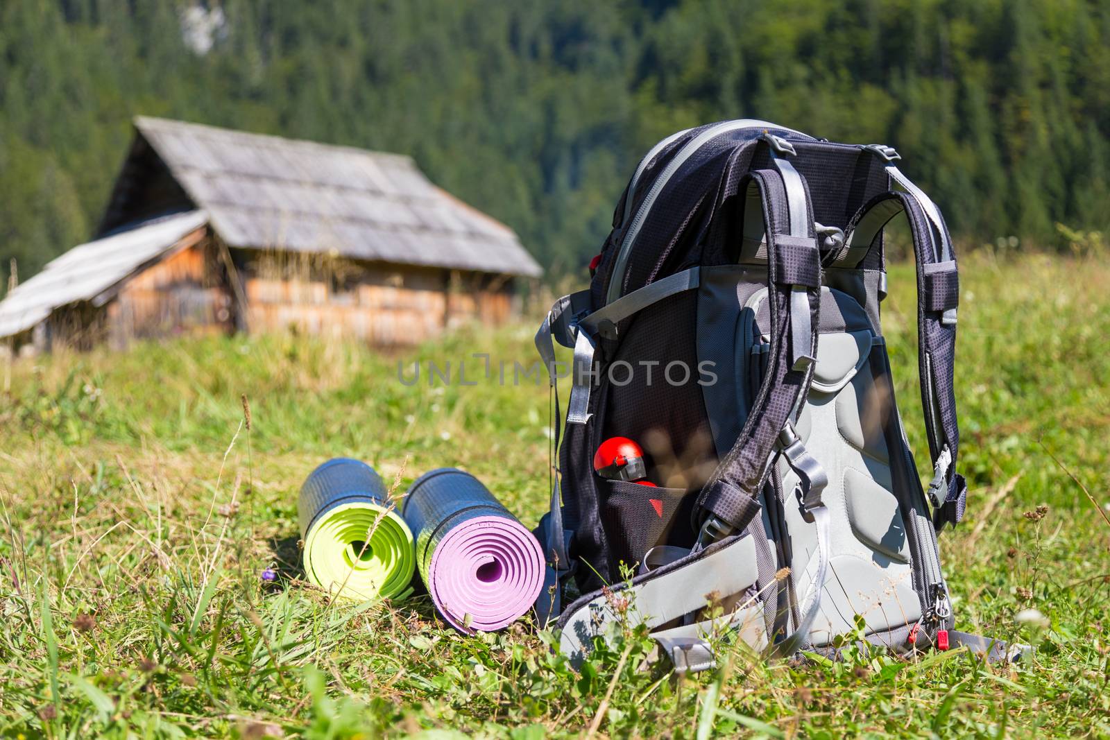 Backpack and yoga mats on mountain meadow with traditional wooden shepherd's huts, Alps, Slovenia.