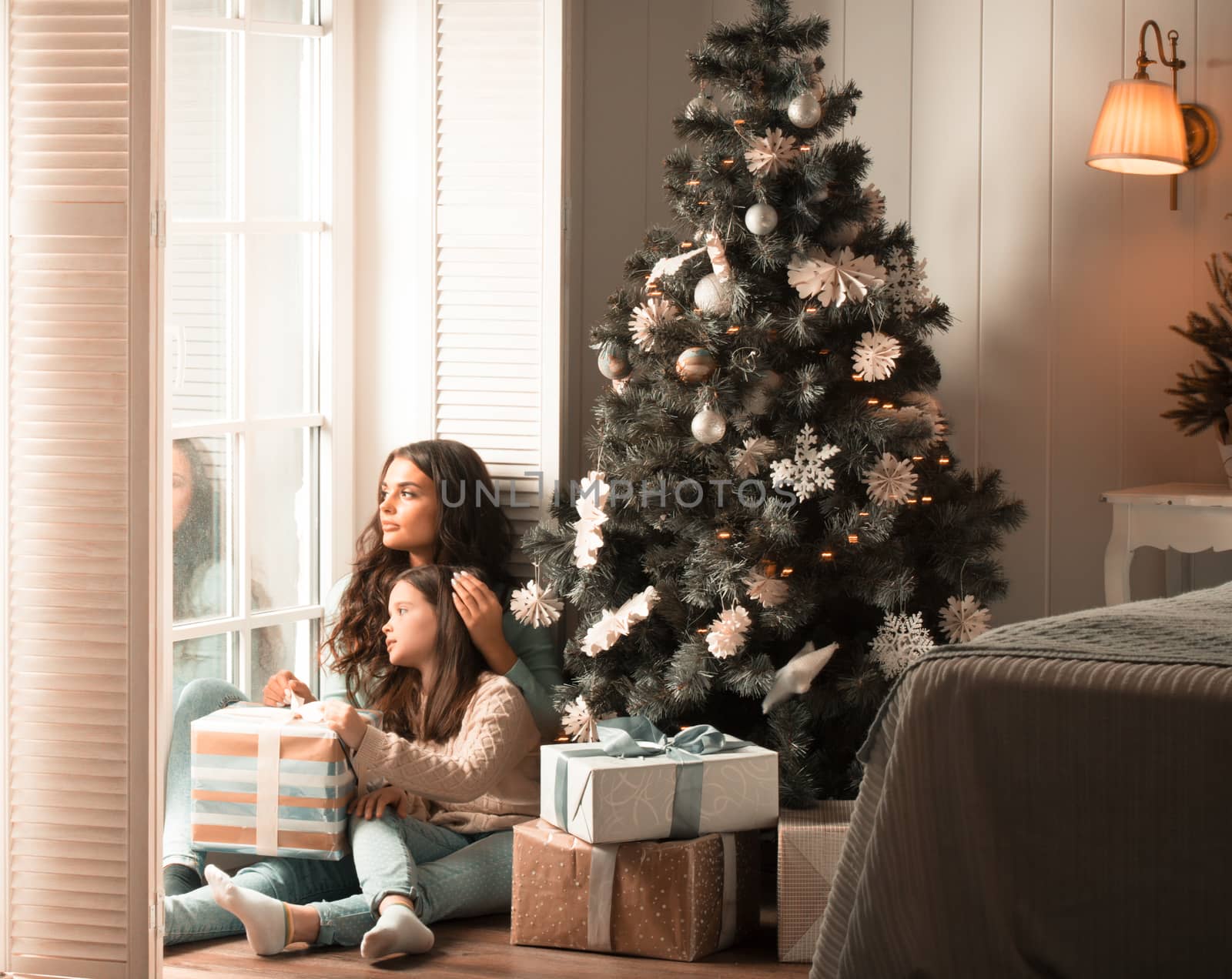 Mother and daughter unwrapping a gift sitting on the floor near christmas tree