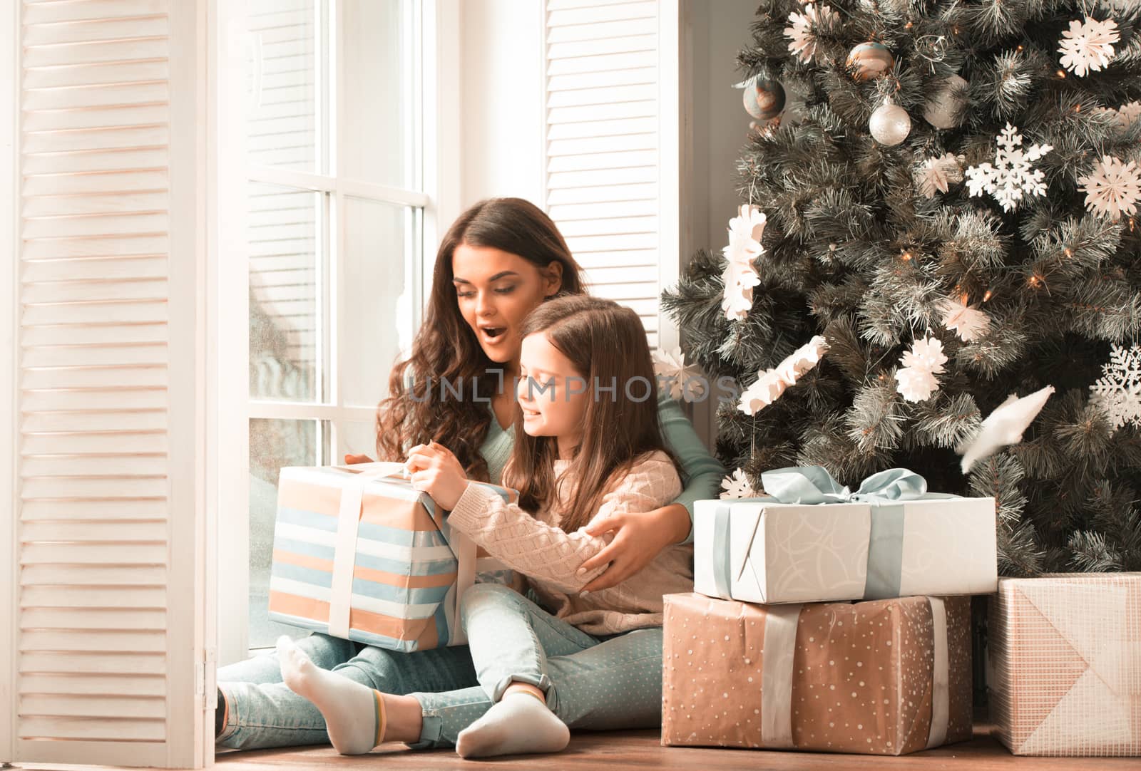 Mother and daughter unwrapping a gift sitting on the floor near christmas tree