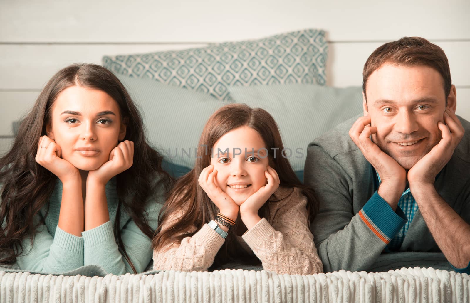 Family portrait of happy parents and their daughter laying on bed at home