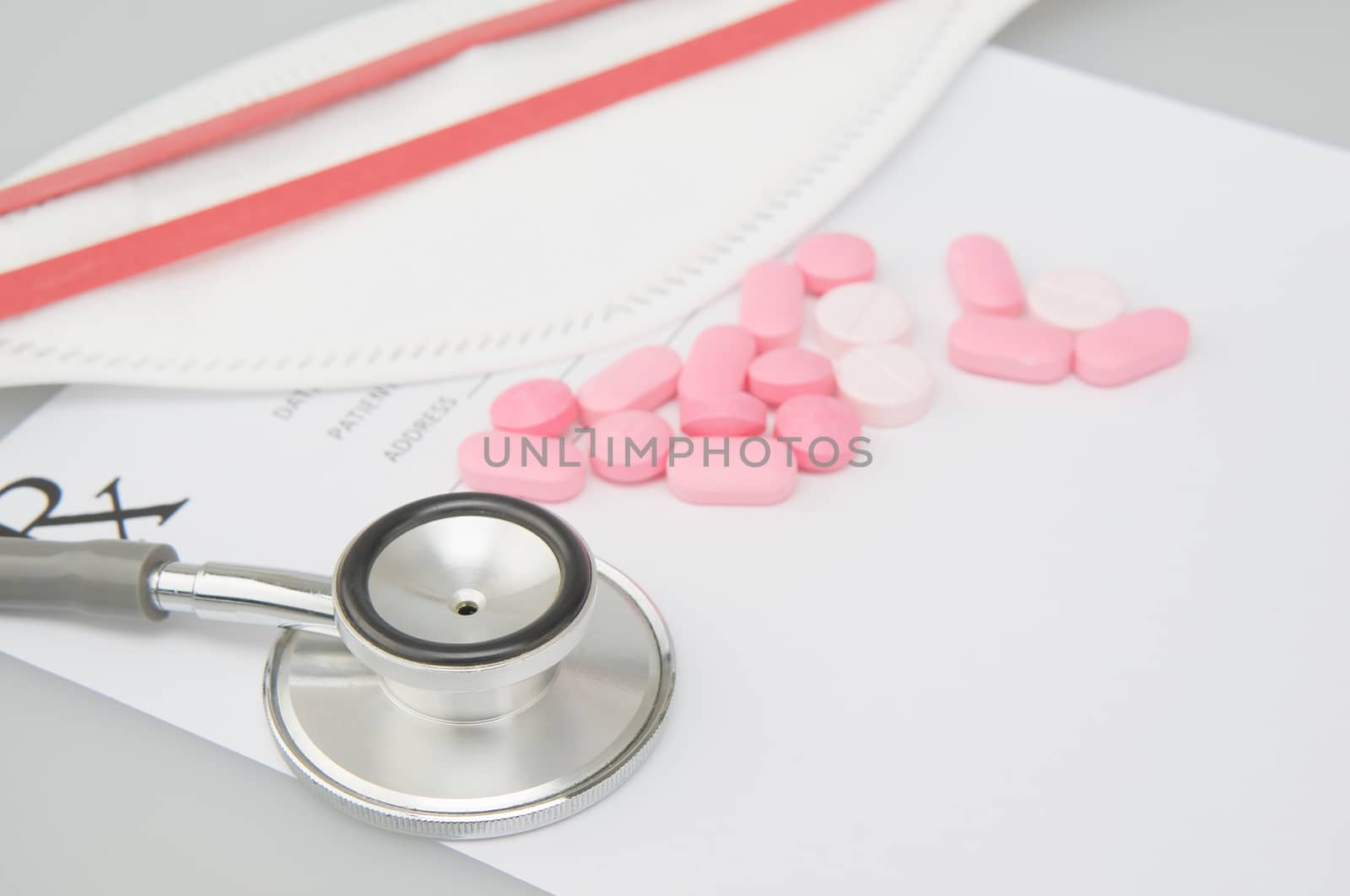 Close up old silver medical stethoscope have blur pink pills and mask on rx prescription form with white background and copy space. Healthcare and medical concept photography.