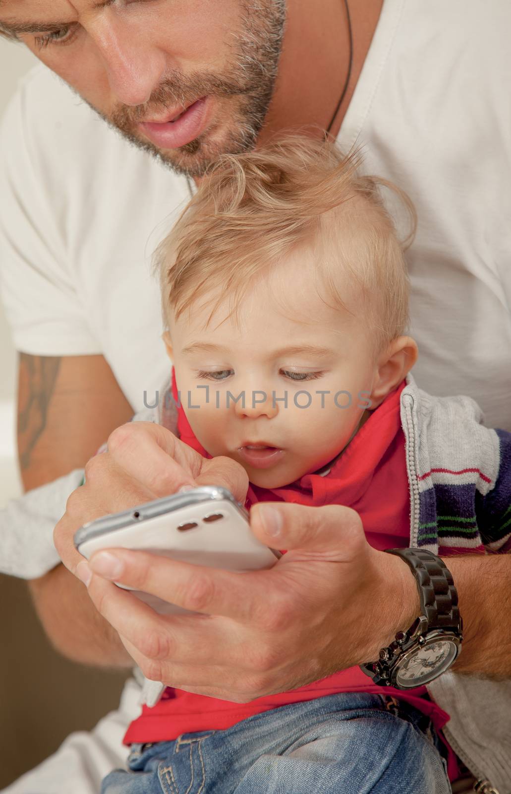 A little baby boy is amazed, looking at his father s mobile phone.