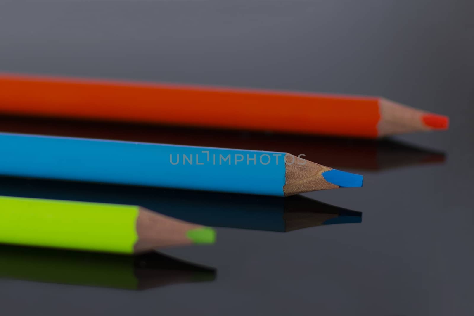 Multicolor pencils lie with reflection on black plexiglass