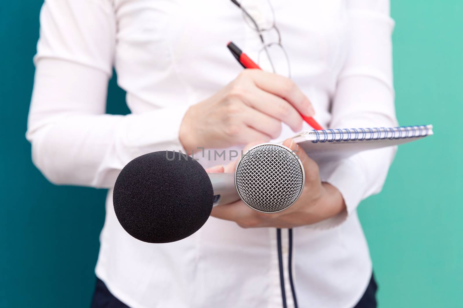 Female reporter taking notes and holding microphones at press conference