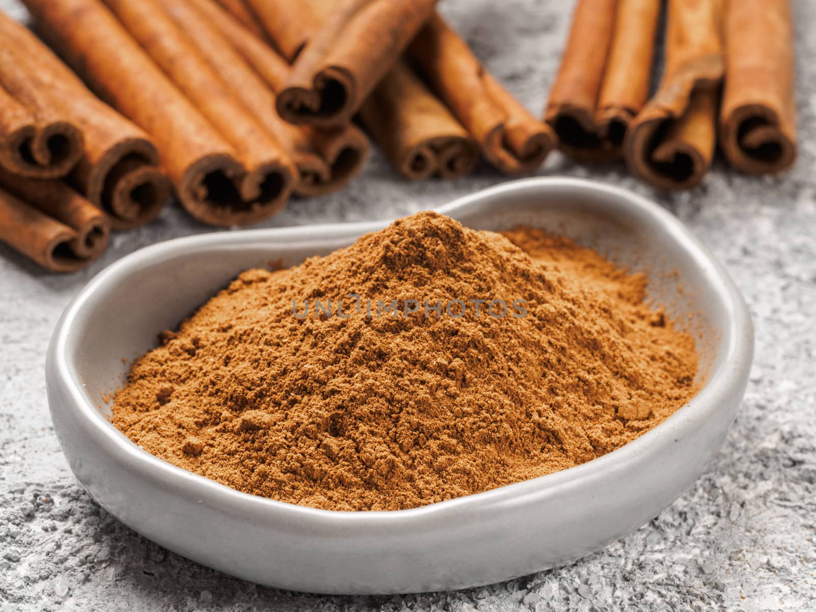 Close up view of ground cinnamon in trendy plate and cinnamon sticks on gray cement background