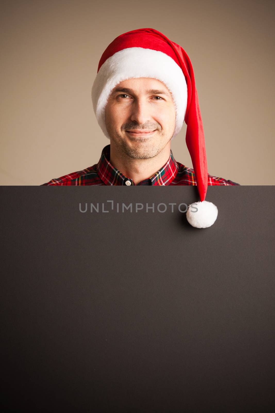 Man wearing santa christmas hat holding and pointing blank billboard or placard sign copy space for text advertising