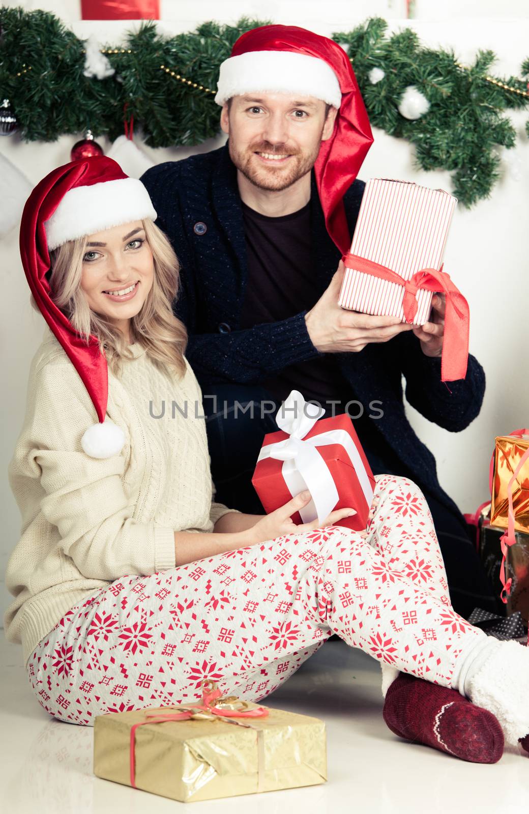 Couple in love sitting next to a nicely decorated Christmas tree, hloding Christmas gifts and smiling