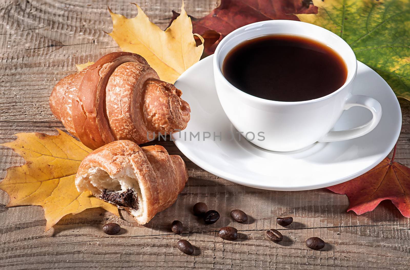 Coffee with a croissant on a wooden table. Grains of coffee and maple leaves on the table.